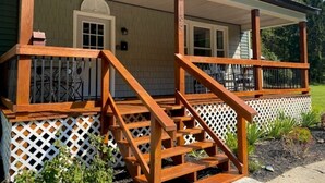 A wooden deck with a white lattice fence, a covered porch, and a door with a window. - Spacious PA Wilds Getaway! Water views, firepit w/ covered patio (Driftwood)