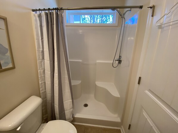 A bathroom with a shower, toilet, and a window above the shower.