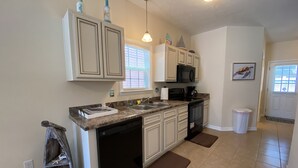 A kitchen with white cabinets, a black dishwasher, a microwave, and a sink. There are brown mats on the floor, and a trash can is visible. - 2 Bed, 2 Bath Topsail Cottage—Walk to the beach! (Myrtle Beach)