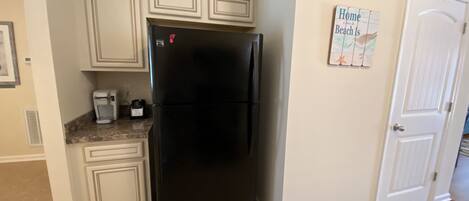 Eine Küche mit einem schwarzen Kühlschrank, einer Kaffeemaschine und einem Rettungsring auf den Schränken. Eine Tür mit einem Schild an der Wand.