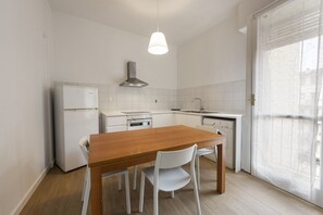 A modern kitchen with white cabinetry, a wooden dining table, and a hanging light fixture.