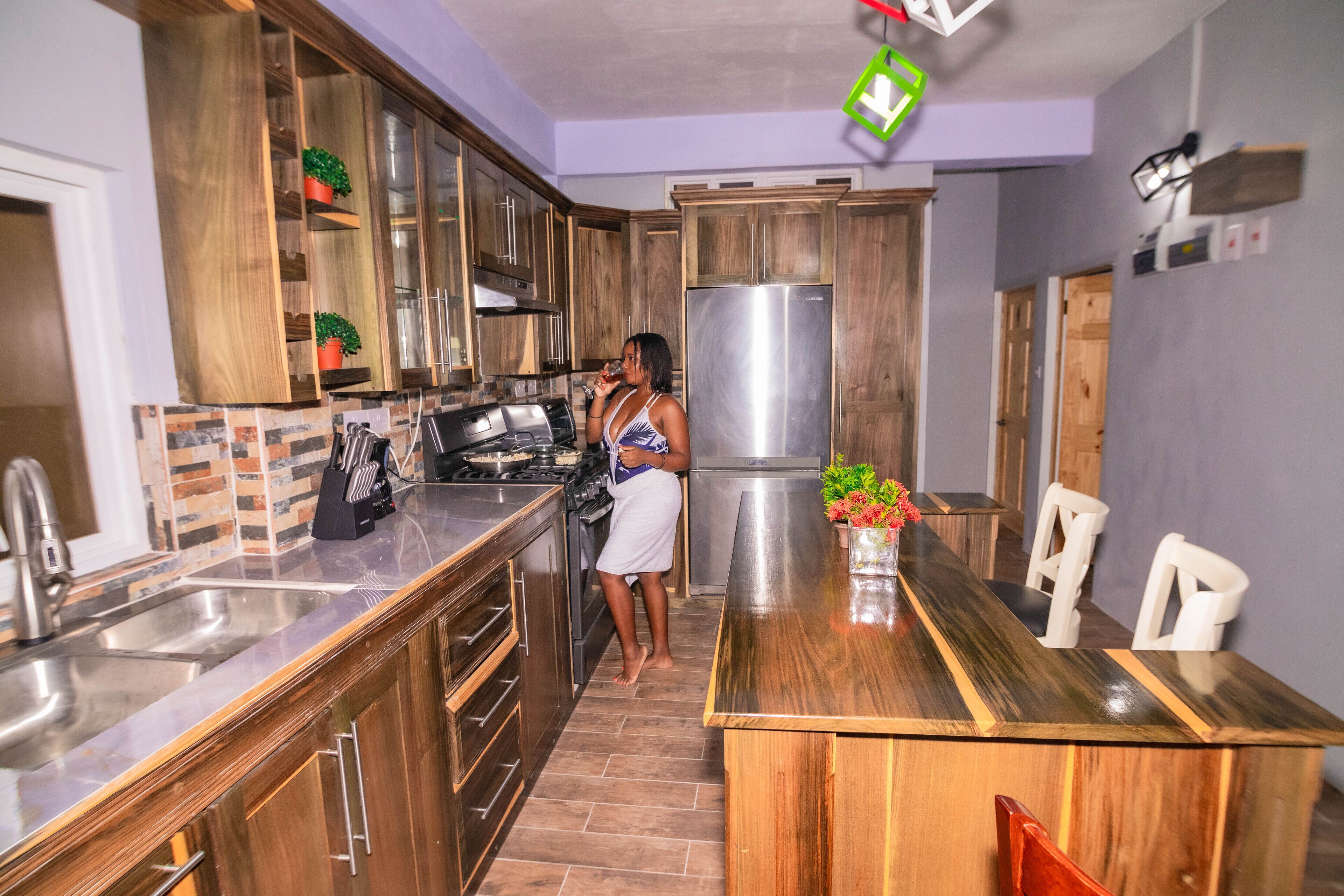A modern kitchen with wooden cabinets, a stainless steel refrigerator, and a dining area with a wooden table and chairs.