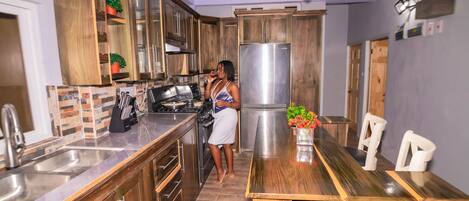 A modern kitchen with wooden cabinets, a stainless steel refrigerator, and a dining area with a wooden table and chairs.