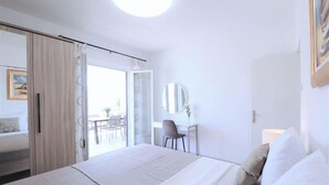 A hotel room with a bed, a desk with a chair, a mirror, and a view of the outside. - Luxury Beachfront Villa With Pool for two Families (Okrug)