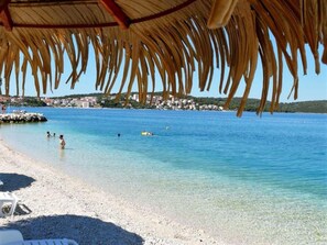 Une plage avec une structure dotée d’un toit de chaume, une eau d’un bleu limpide et une plage de galets.