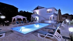 A modern villa with a swimming pool, lounge chairs, and a covered seating area. - Luxury Beachfront Villa With Pool for two Families (Okrug)
