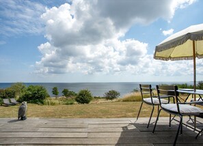 An outdoor deck with a view of the sea, a wooden table with chairs, and an umbrella. - Architect designed holiday home with sea view (Gudhjem)