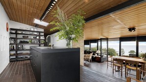 Une cuisine moderne dotée d’un îlot central, d’un plafond en bois et de grandes fenêtres offrant une vue panoramique.