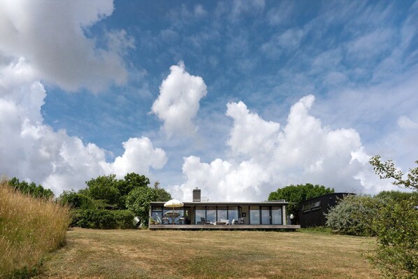 A modern house with a flat roof, large windows, and a covered outdoor seating area. - Architect designed holiday home with sea view (Gudhjem)