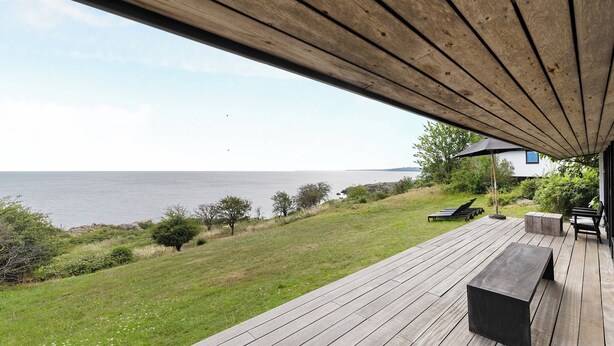 Une terrasse en bois avec un banc, une table et une vue sur la mer.