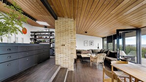 Une cuisine moderne avec un pilier en briques, un plafond en bois et un coin repas comprenant une table et des chaises.