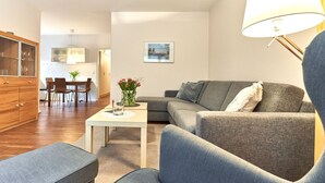 A modern living room with a grey sofa, a small white table with a vase of flowers, and a wooden cabinet.