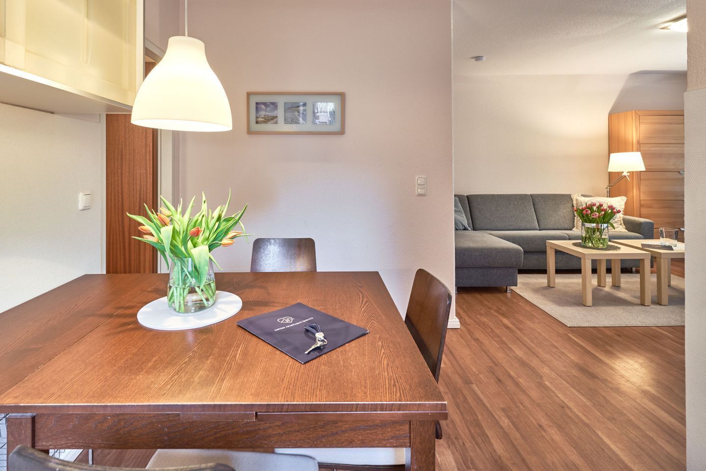 A modern dining area with a wooden table, chairs, a vase of flowers, and a pendant light.