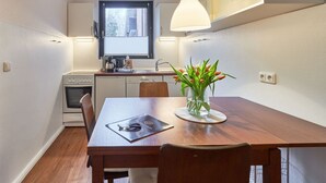 A compact kitchen with a dining area, a window with blinds, and a vase with flowers on the table.