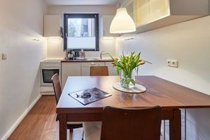 Une cuisine compacte avec un coin repas, une fenêtre avec des stores et un vase de fleurs sur la table.