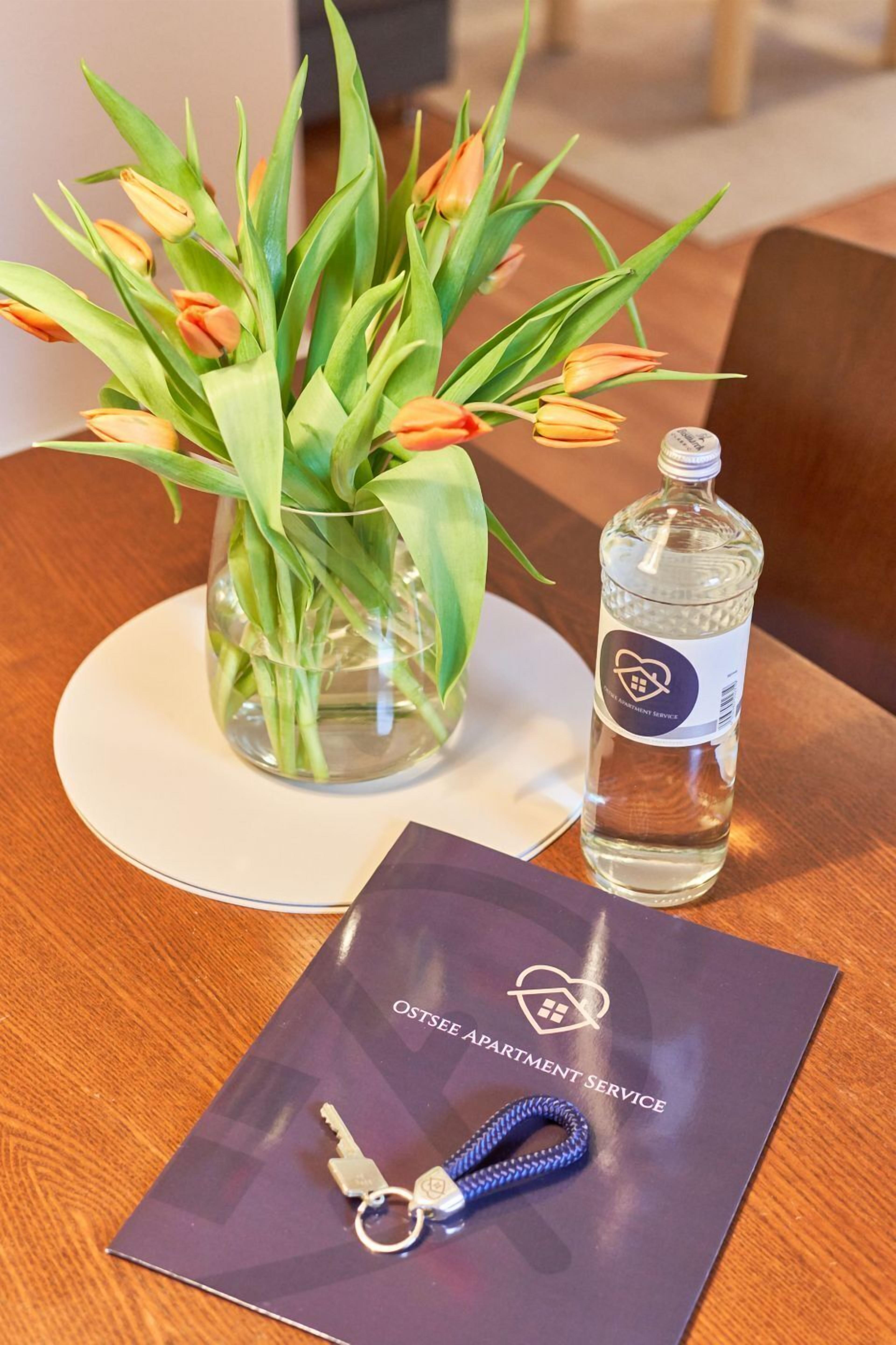 Una mesa de madera con un florero transparente que contiene tulipanes anaranjados, una botella de agua y un llavero con un candado sobre una tarjeta azul oscuro.