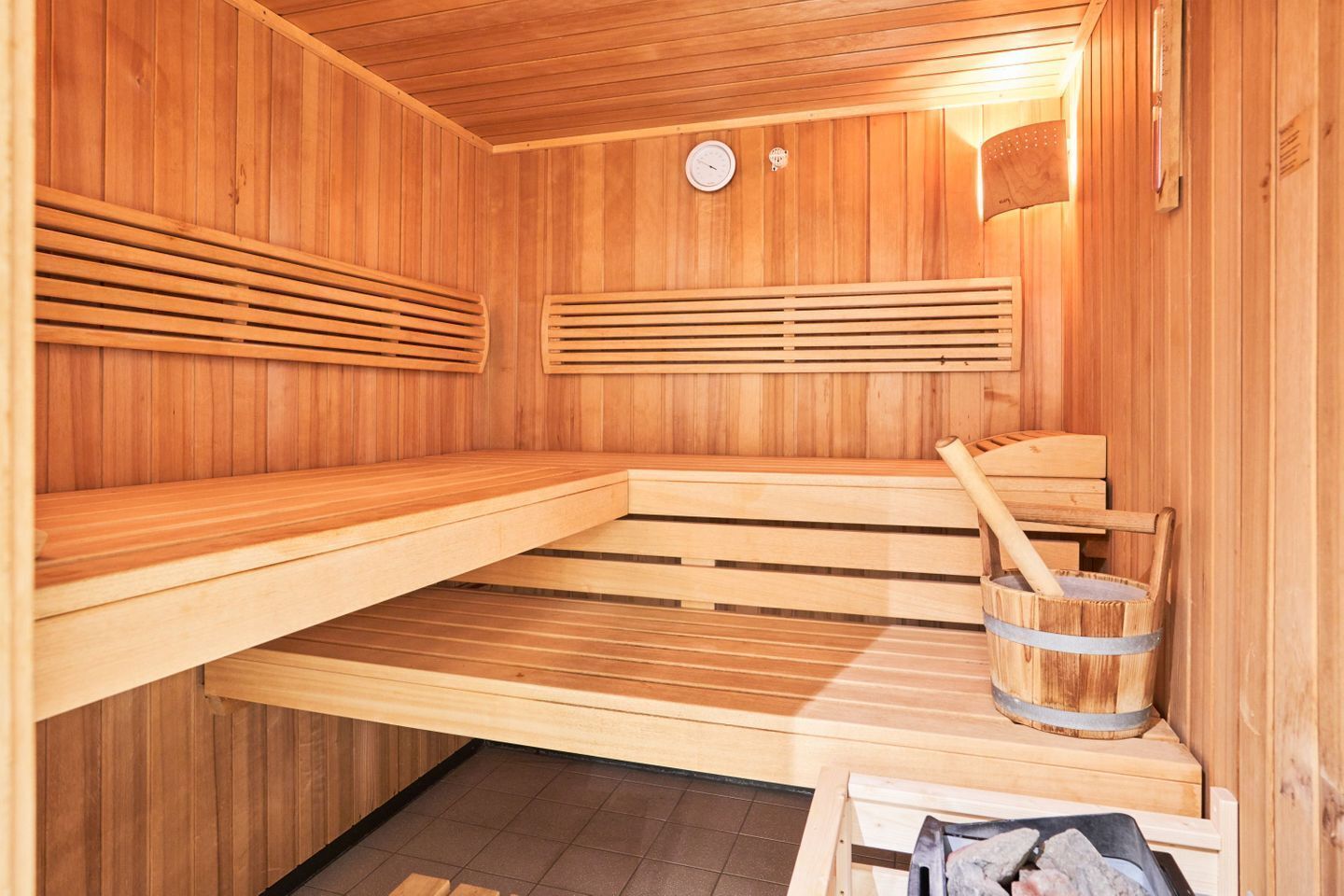 Una sauna de madera con bancos, un balde de madera y un reloj en la pared.