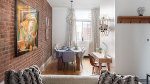 Comedor con pared de ladrillo, una mesa lista para cuatro comensales y una ventana con cortinas.