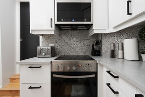 A kitchen with white cabinets, a built-in oven, a microwave, and a patterned backsplash.