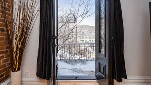 Puerta abierta que da a un balcón con vistas a un edificio y árboles desprovistos de hojas.