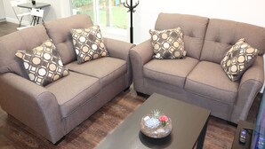 Two sofas with patterned cushions, a coffee table with a decorative bowl, and a dining area with chairs and a table. - Spacious 3 Bedroom walkout Basement Apartment (Ajax)