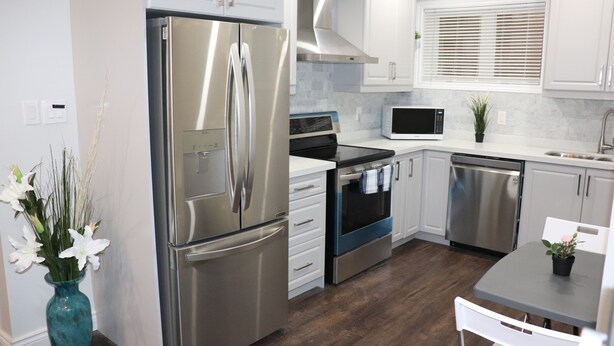 A modern kitchen with stainless steel appliances, white cabinets, and a wooden floor. - Spacious 3 Bedroom walkout Basement Apartment (Ajax)