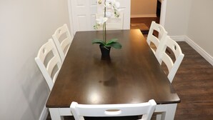 A dining table with chairs, a potted orchid, and a door in the background. - Spacious 3 Bedroom walkout Basement Apartment (Ajax)