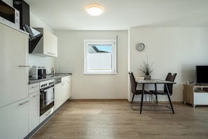 Una cocina moderna con armarios blancos, horno empotrado y comedor con mesa y sillas.
