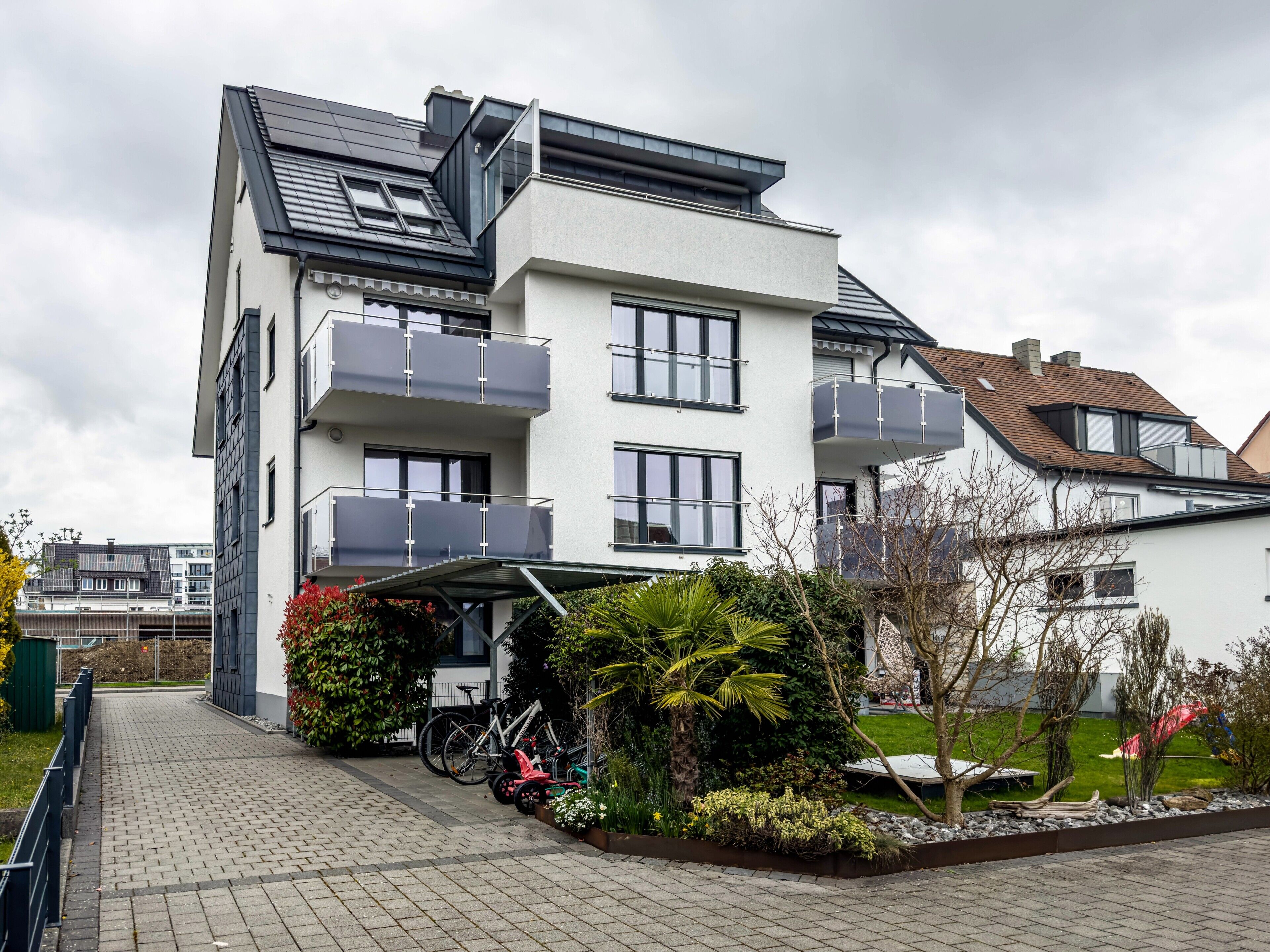 Ein modernes Wohnhaus mit zwei Etagen, Balkonen, einer überdachten Auffahrt und einem Garten.