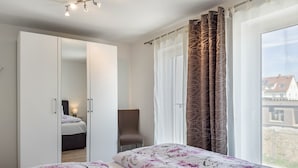 Un dormitorio con cama, una silla, un armario y una ventana con cortinas.