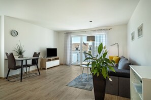 Ett modernt vardagsrum med en matplats, en platt-TV, en krukväxt och en soffa med kuddar.