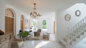 A spacious, well-lit interior with a chandelier, a staircase, and a seating area with a view of the outdoors. - Arpo Pool Villa Riverside Bangkok | 3-Bedroom Private Villa Near MRT & Iconsiam (Bangkok)