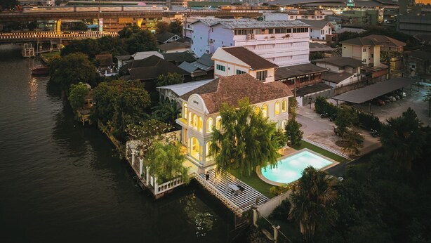 A waterfront property with a swimming pool, a large house with a balcony, and a city skyline in the background. - Arpo Pool Villa Riverside Bangkok | 3-Bedroom Private Villa Near MRT & Iconsiam (Bangkok)