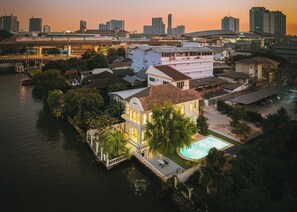 Een pand aan het water met een zwembad, een groot huis met een balkon en een stadsachtergrond.