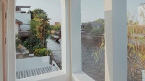 A balcony with arched windows overlooking a canal with buildings and greenery. - Arpo Pool Villa Riverside Bangkok | 3-Bedroom Private Villa Near MRT & Iconsiam (Bangkok)