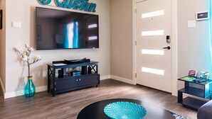 Una sala de estar con un televisor de pantalla plana, una consola oscura, un florero azul turquesa e una puerta con interruptor de luz.