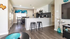 Una cocina moderna con armarios blancos, una isla central y una zona de comedor con mesa y sillas.