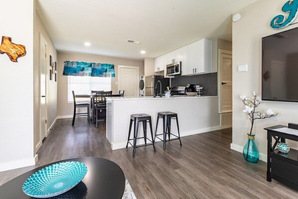 Una cocina moderna con armarios blancos, una isla central y una zona de comedor con mesa y sillas.