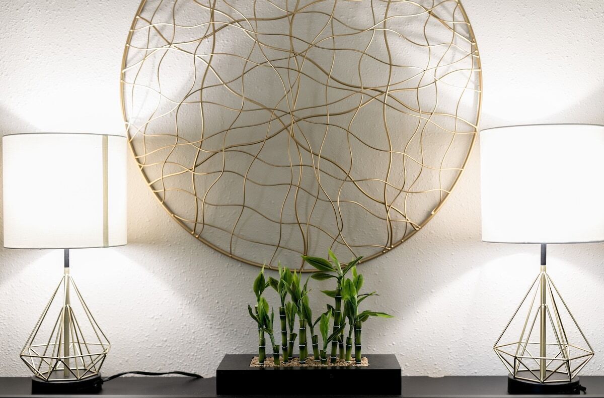 Un interior modern amb dues làmpades de terra geomètriques, una gran obra d'art abstracta a la paret i un arranjament de plantes de bambú petit sobre un pedestal negre.