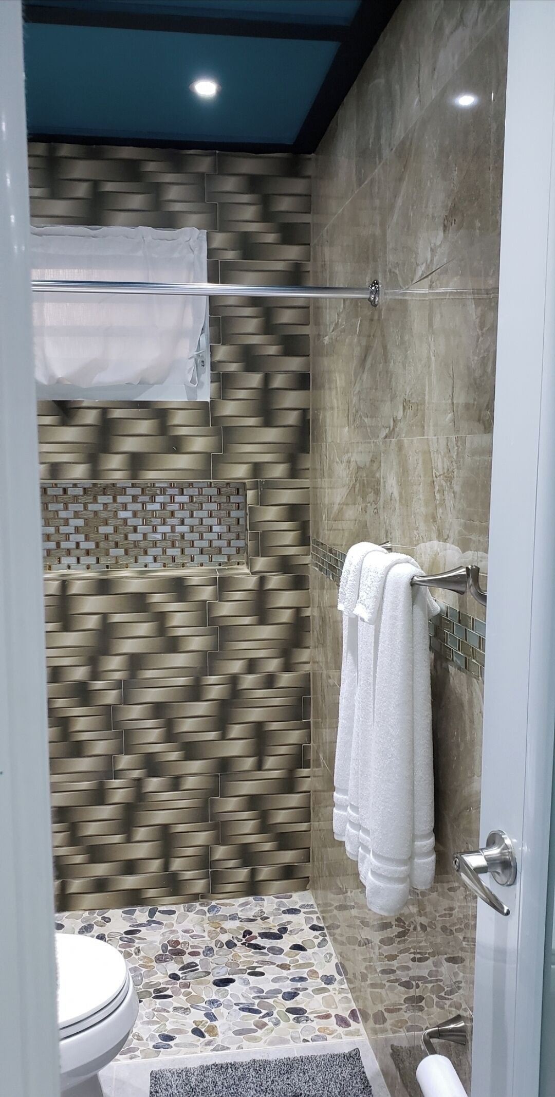 A modern bathroom with a stone mosaic floor, a shower with a glass door, and a towel rack.