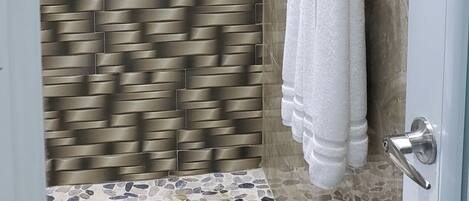 A modern bathroom with a stone mosaic floor, a shower with a glass door, and a towel rack.