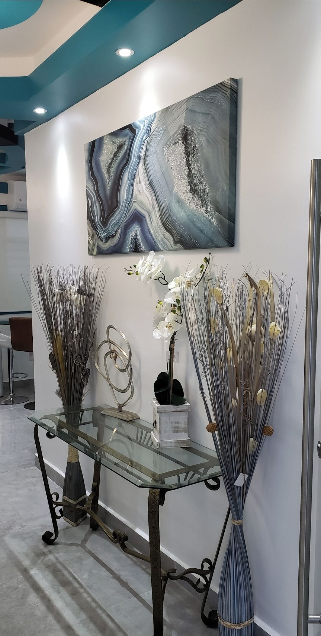 A reception area with a glass-top table displaying decorative items, a wall-mounted abstract painting, and a door to the right.