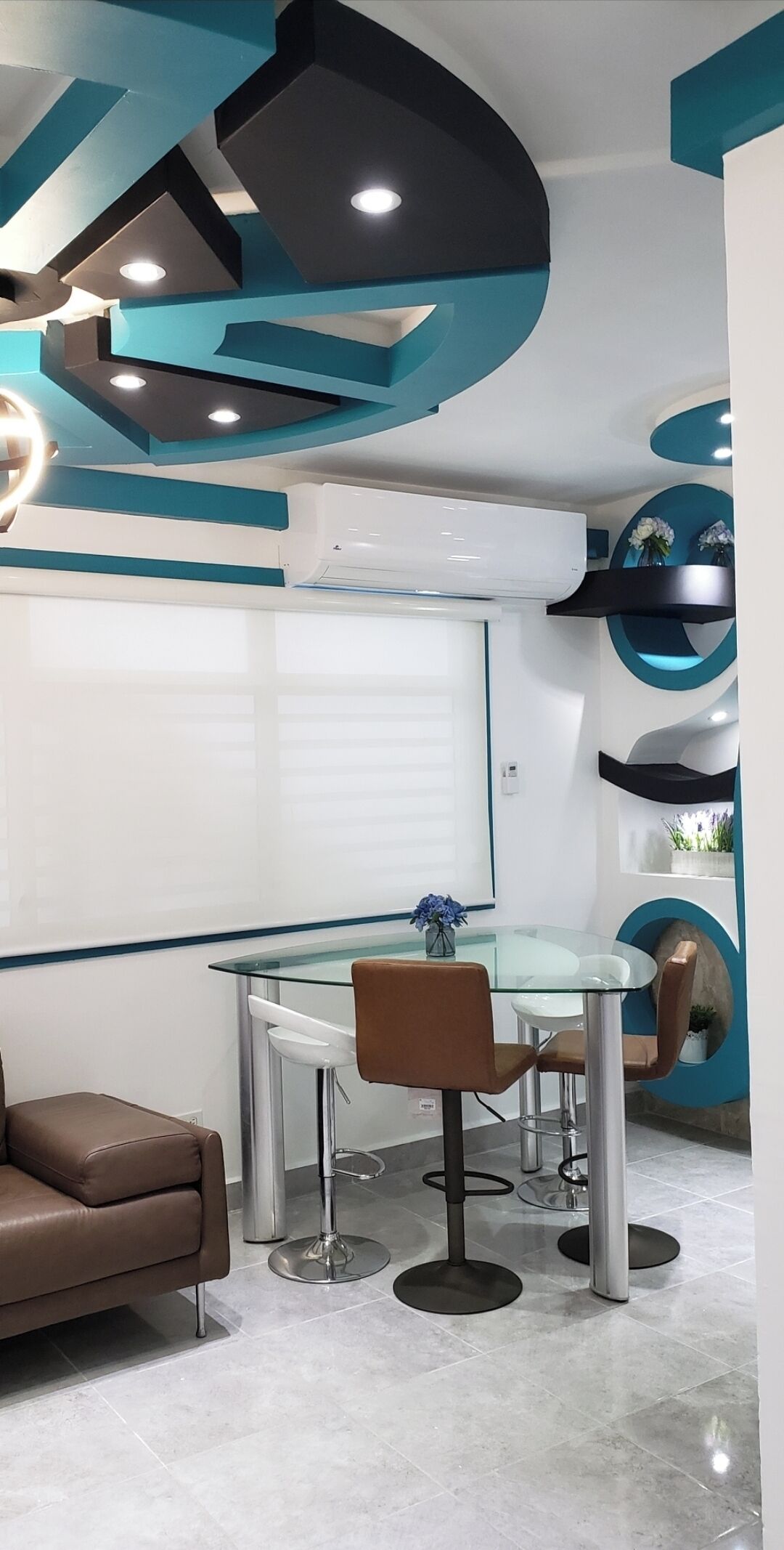 Un comedor moderno con mesa de vidrio, sofá de cuero marrón y paredes de acento color turquesa.
