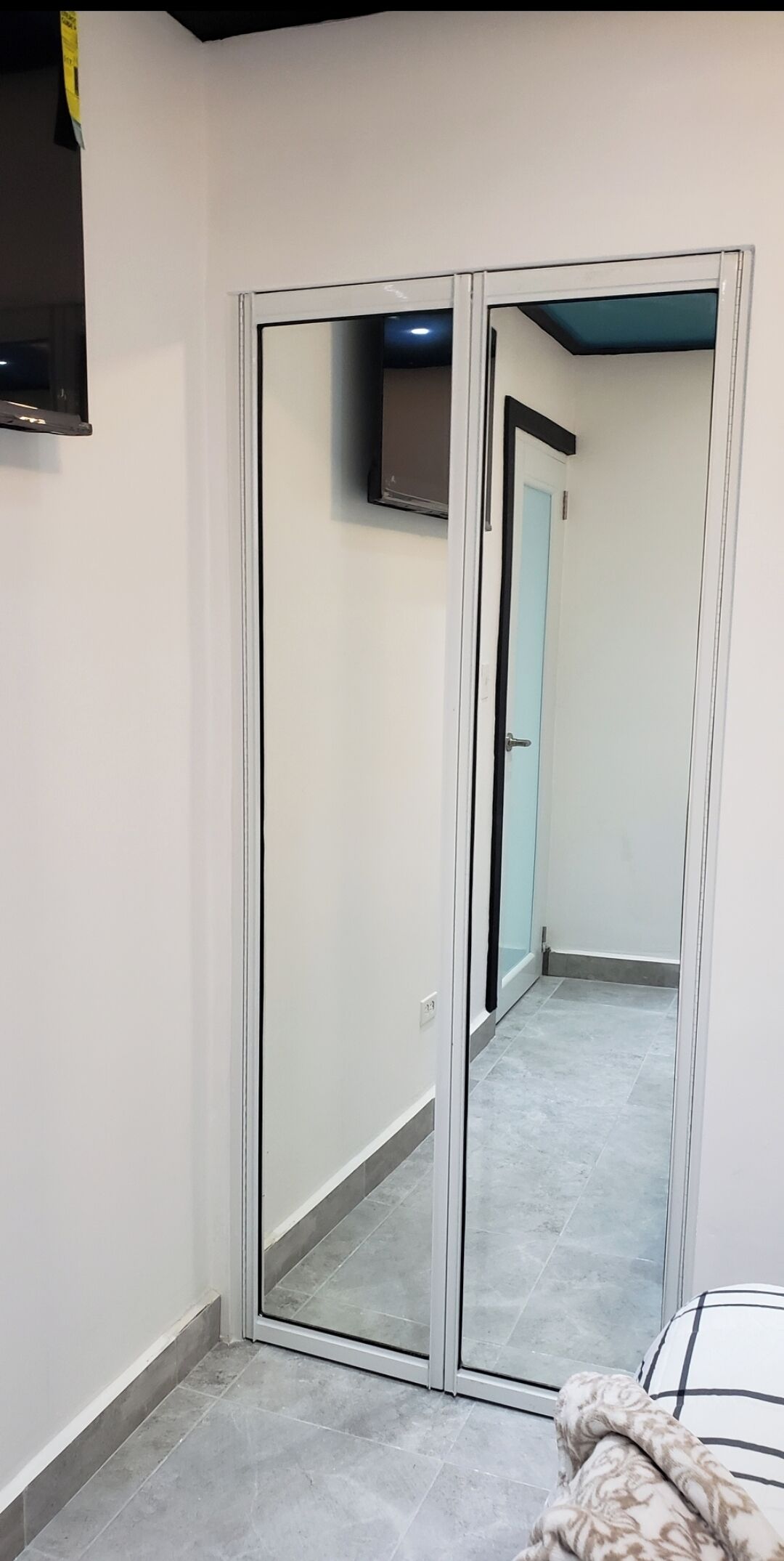 Una habitación con armario de puertas correderas, un televisor de pantalla plana montado en la pared y un cojín estampado sobre la cama.