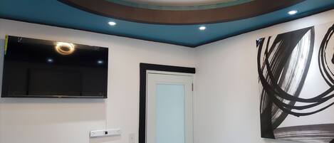 A modern room with a flat-screen TV mounted on the wall, a door with a light blue panel, and a large abstract painting on the wall.