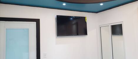 A room with a flat-screen TV mounted on the wall, a door with a light blue panel, and a white wall.