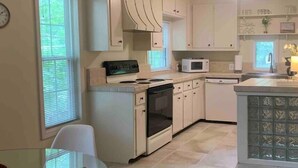 A compact kitchen with white cabinets, a microwave, a stove, and a dishwasher. - Mountainside Cottage (Hot Springs)