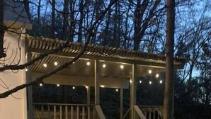 A covered outdoor area with a wooden deck, stone steps, and string lights. - Mountainside Cottage (Hot Springs)