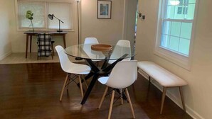 A dining area with a glass table surrounded by white chairs and a bench. - Mountainside Cottage (Hot Springs)