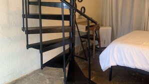 A room with a spiral staircase, a bed, a small table, and a wall-mounted mirror. - Mountainside Cottage (Hot Springs)
